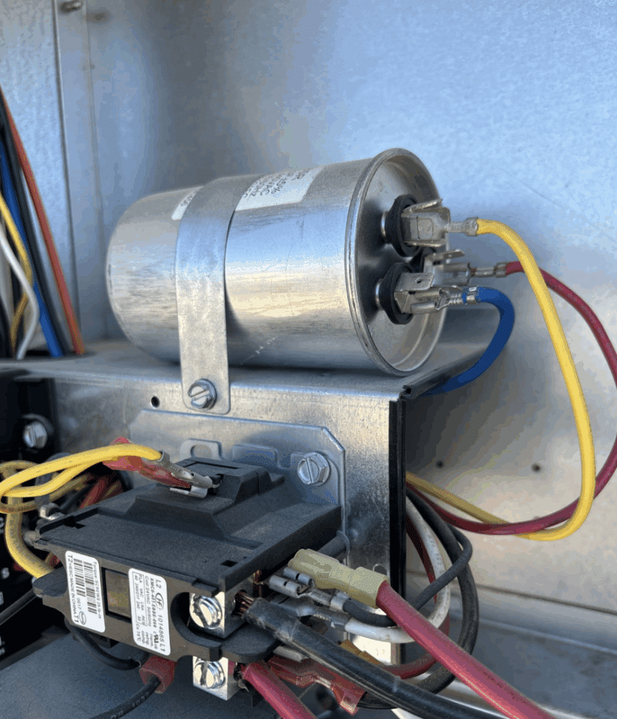 Close-up of HVAC capacitor and contactor with electrical wiring inside an air conditioning unit during system inspection.
